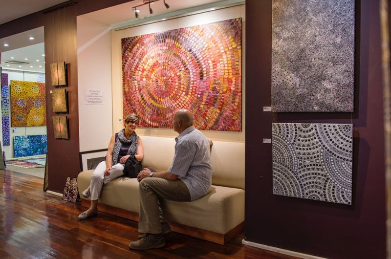 Couple on a seat in front of Aboriginal artworks hanging on gallery wall.